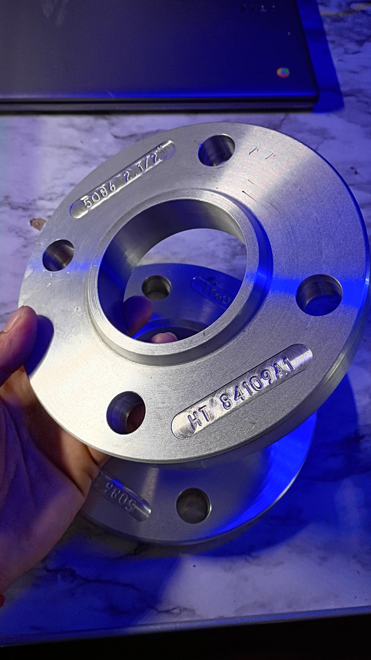 Aluminum wheel spacer with engraved specs, held in hand