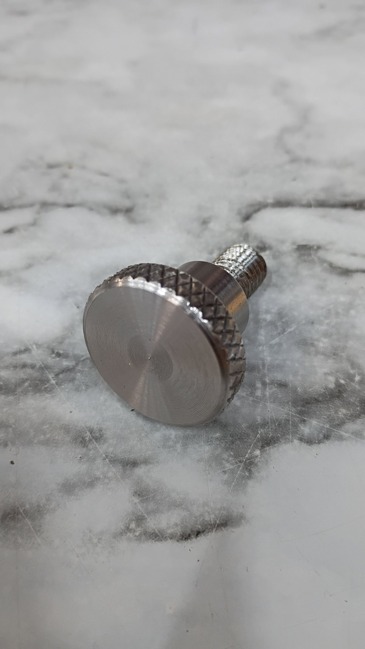 Knurled aluminum thumbscrew on a marble surface